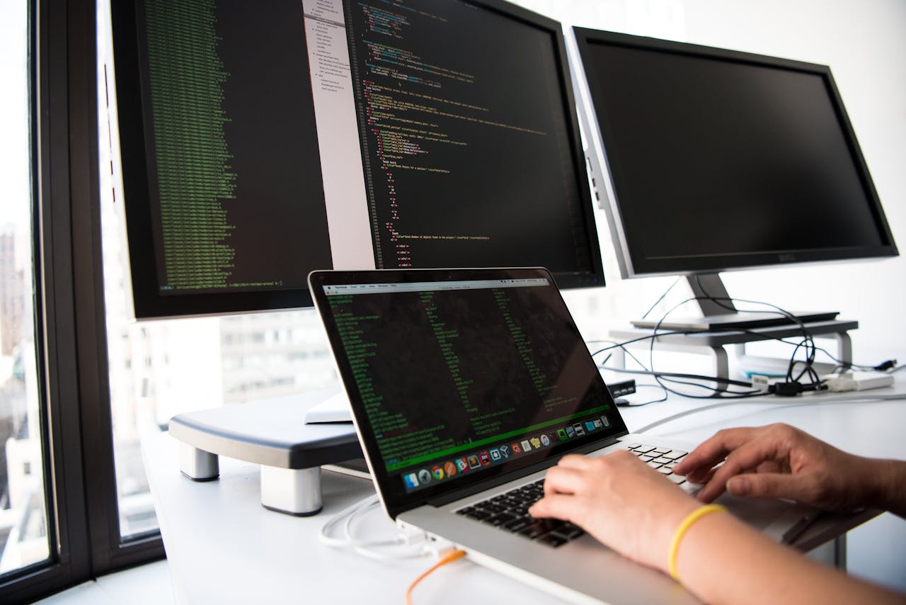 creative A developer writes code on a laptop in front of multiple monitors in an office setting.
